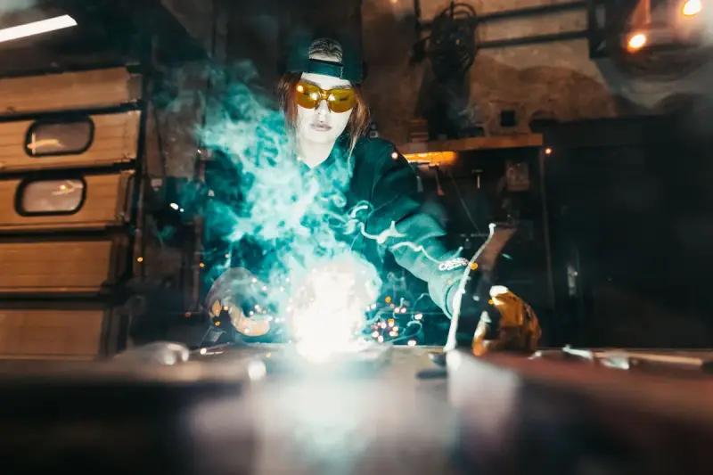 Female welder in protective gear working as sparks fly in a workshop