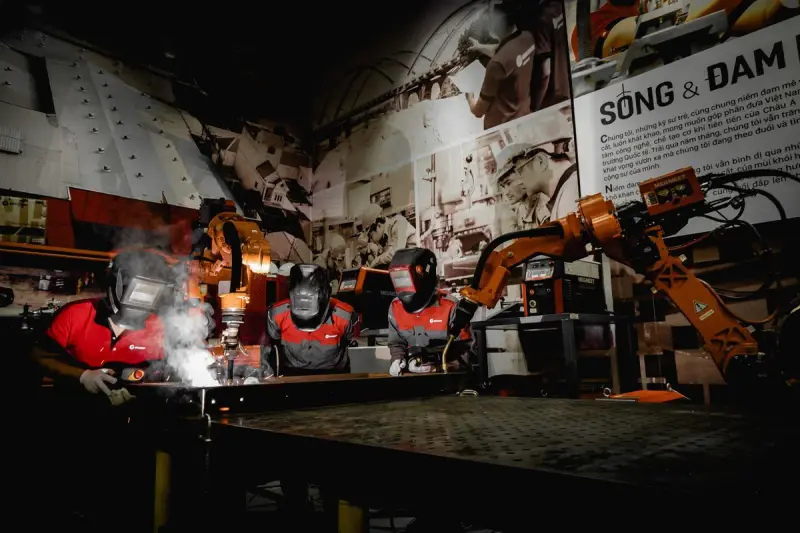 Welders in protective gear working beside robots in an industrial workshop