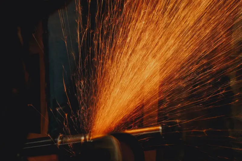 A fan of bright orange sparks flying from a grinder across steel in a dark workshop