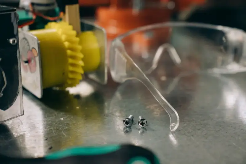 Silver screws lying beside safety glasses on a metal workbench