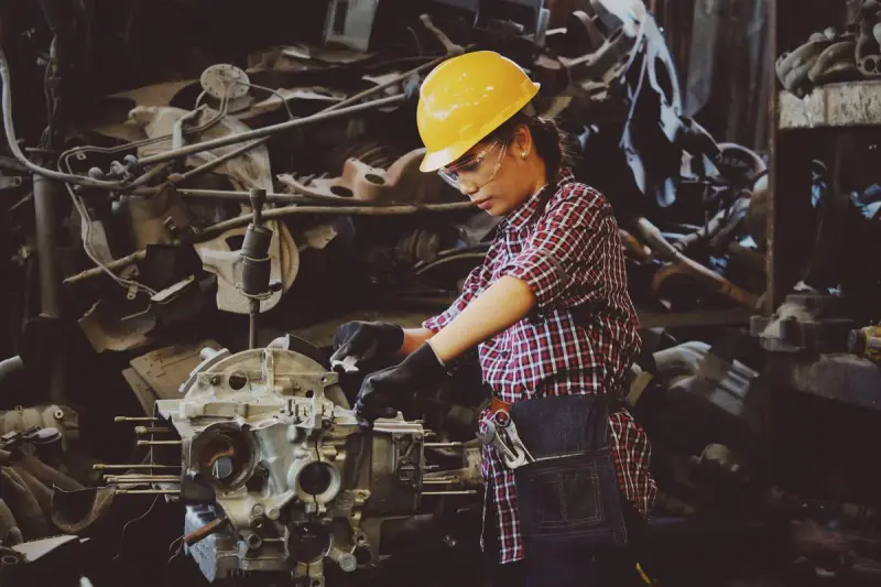 Woman engineer in a yellow hard hat working on a machine part