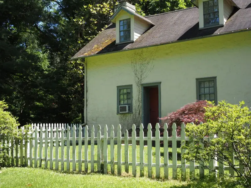White picket fence along the lawn of a cream cottage with a red door
