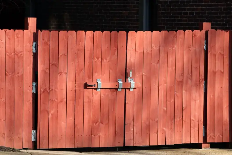 Red-stained wooden double gate with galvanized hinges and a drop-bar latch