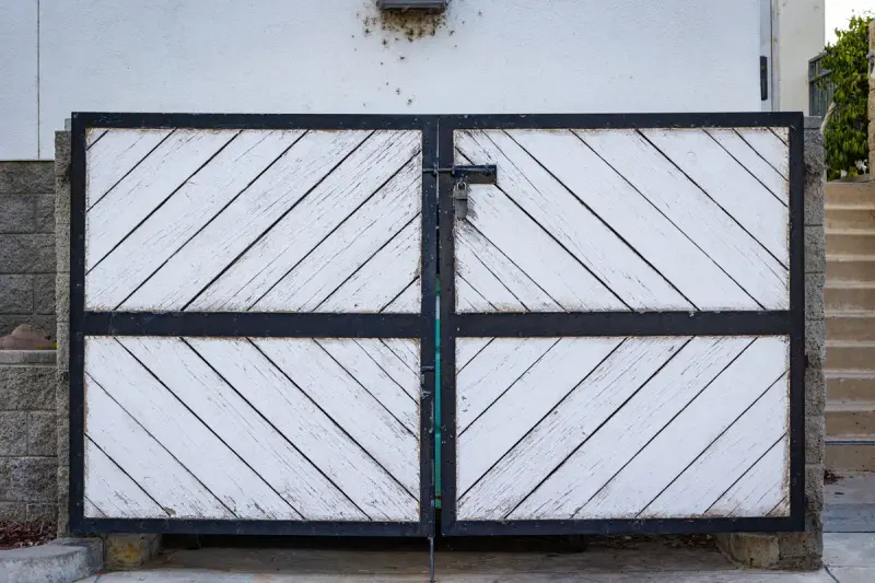 White wooden double gate in a black metal frame with a cane bolt and padlock hasp