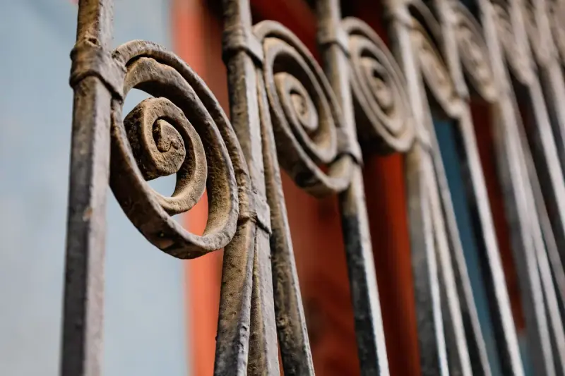 Close-up of scrolled wrought-iron fence pickets in front of a red and blue wall