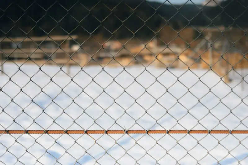 Close-up of chain-link mesh with a horizontal tension wire over a snowy field