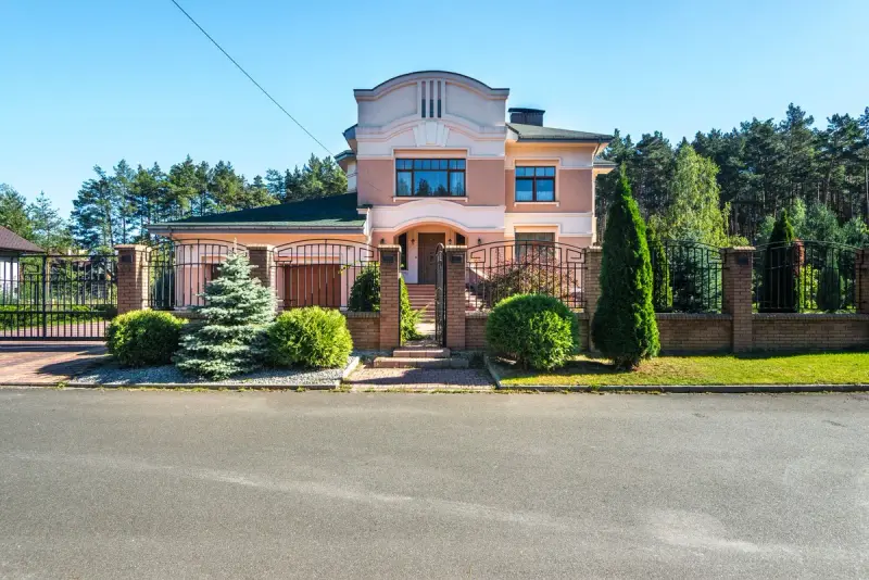 House behind a brick-pillared perimeter fence with black iron panels, a driveway gate and a pedestrian gate