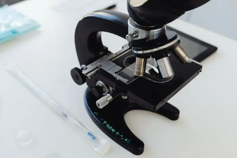 Black laboratory microscope on a white bench beside a pipette