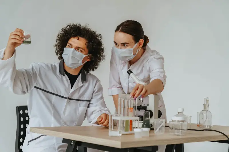 Two scientists in protective masks working with a microscope and test tubes