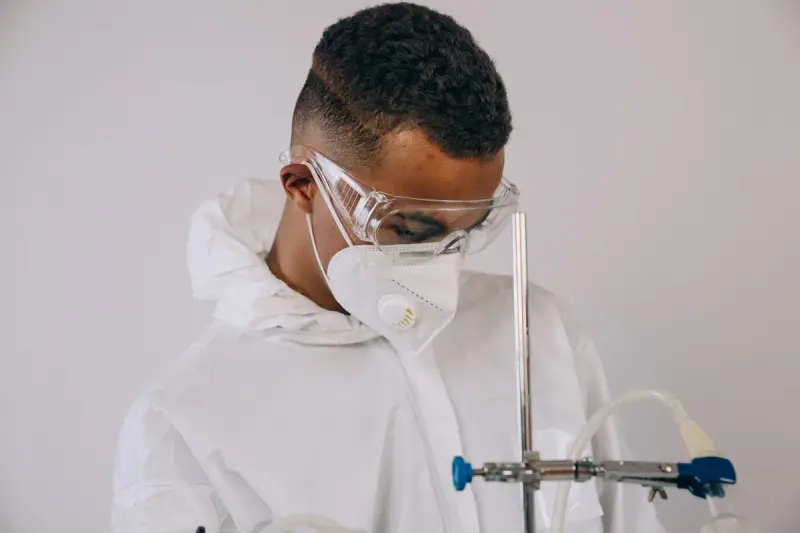 Scientist in coveralls, safety glasses and face mask running an experiment