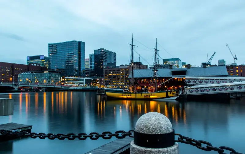 Boston skyline and a historic ship reflected in the harbor at twilight