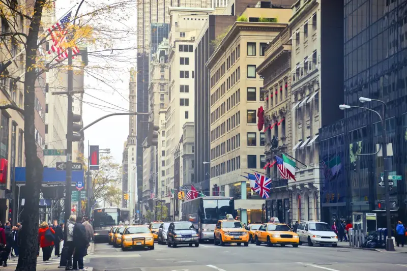 Midtown Manhattan avenue lined with office towers, flags and yellow taxis