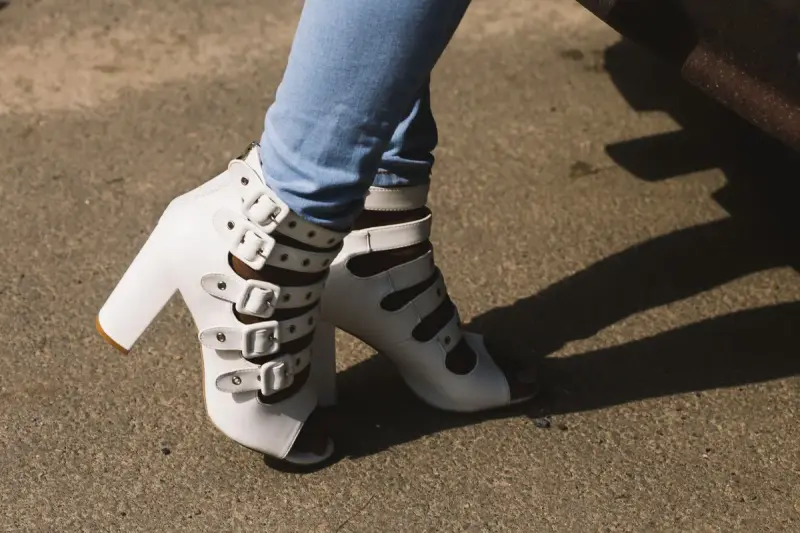White multi-buckle peep-toe block-heel sandals worn with light jeans on pavement