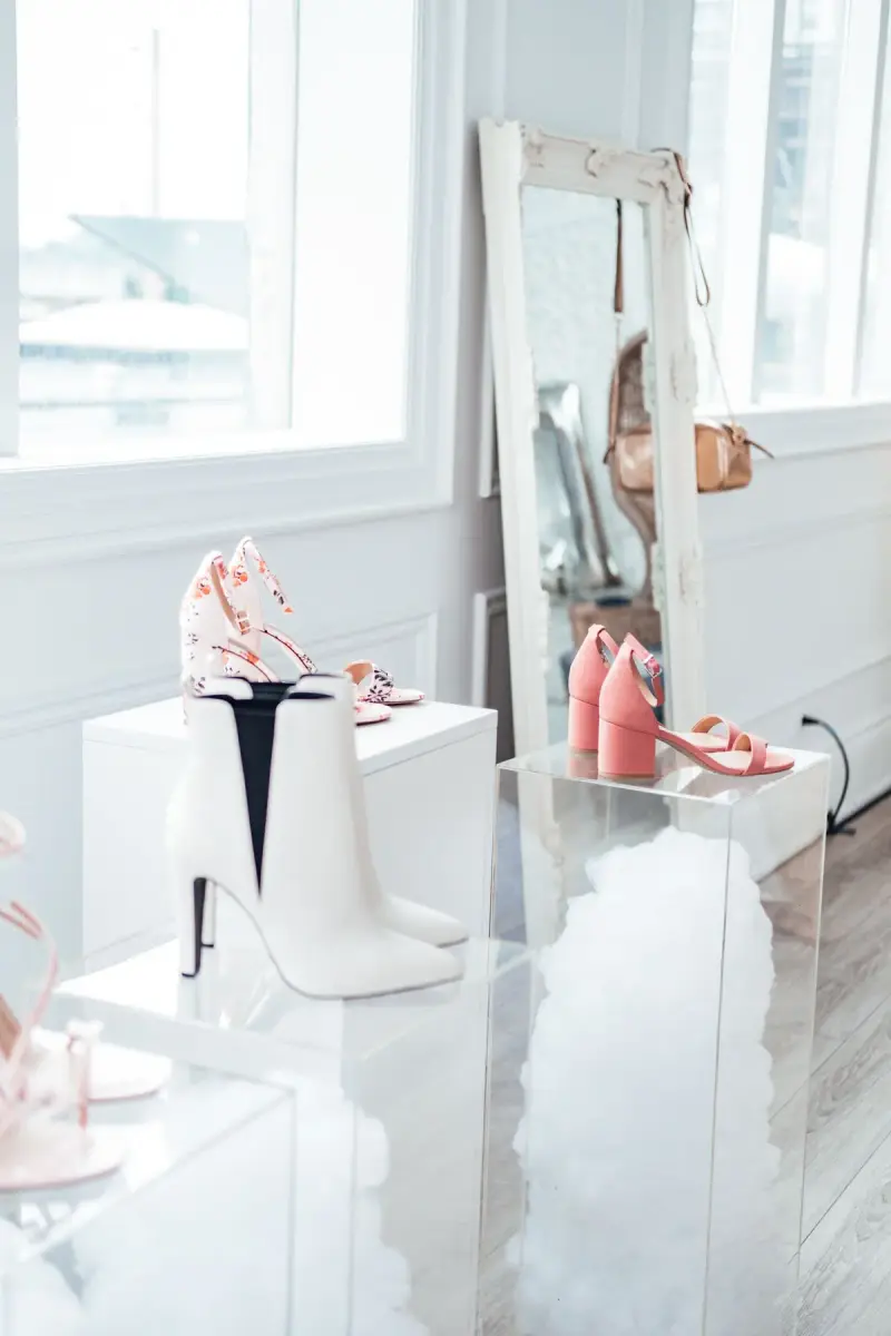Pink heels and white boots on pedestals in a bright boutique