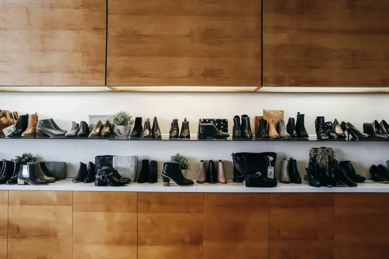 Long wall of women's shoes and boots on lit shelves under wood panels