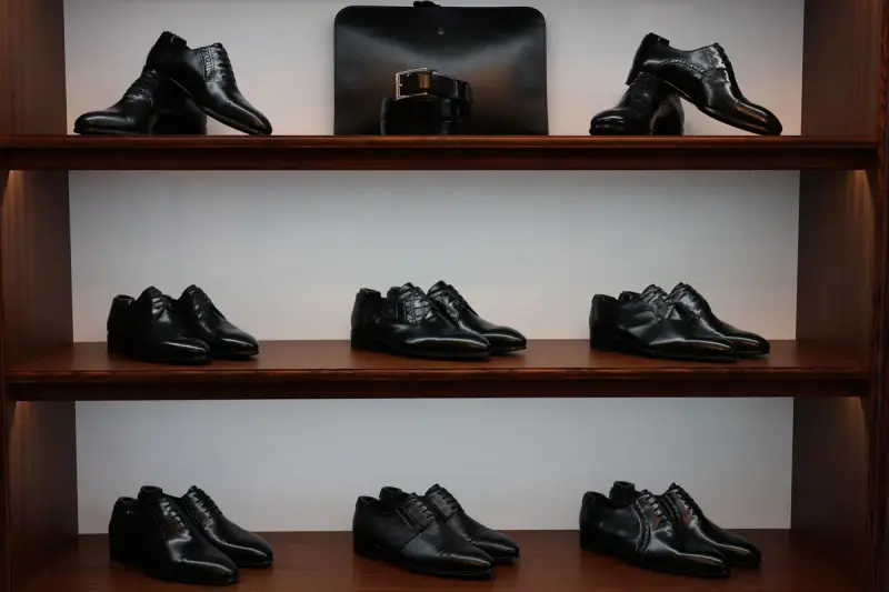 Black leather dress shoes lined up on dark wooden shelves