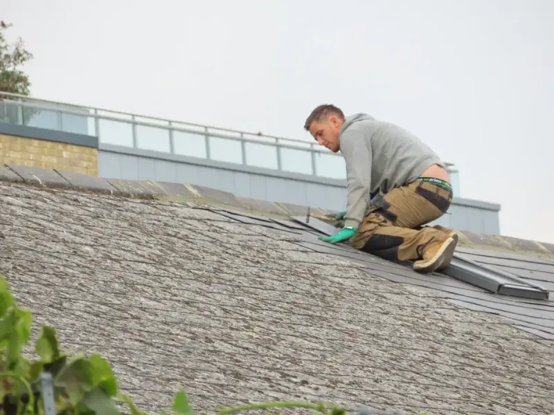 A worker installs roof shingles outdoors.