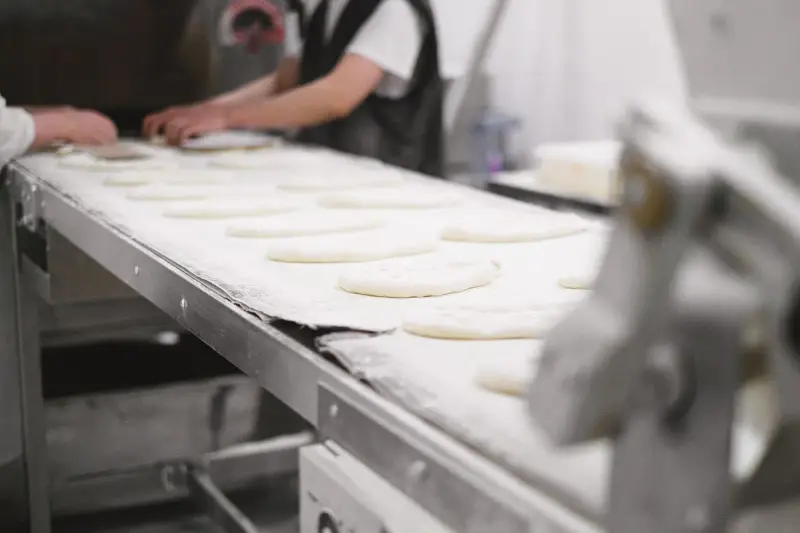 Bakery workers shaping dough pieces on a conveyor in an industrial bakery