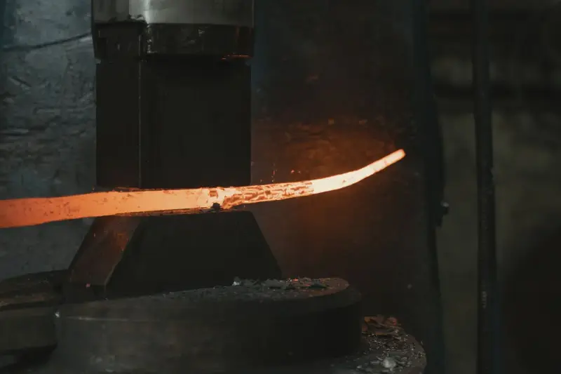 Glowing steel bar being shaped between the dies of a power hammer