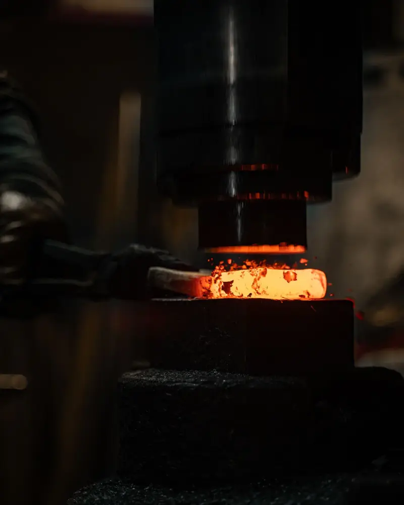 Red-hot billet flattened under a hydraulic press ram with sparks flying