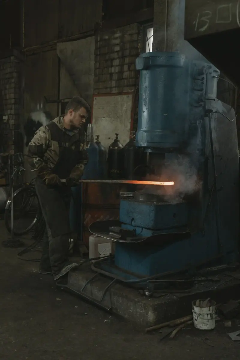 Smith in safety glasses feeding a glowing bar into a blue power hammer