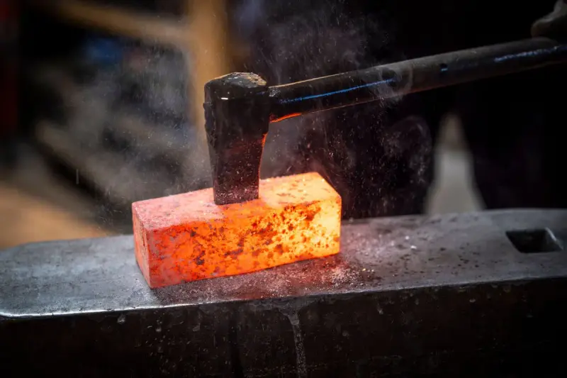 Hammer striking a glowing orange steel billet on an anvil