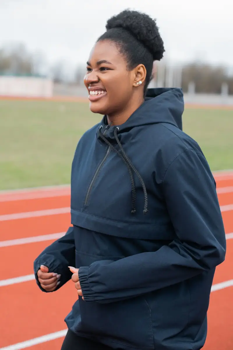 Smiling woman running on a track in a navy hooded anorak