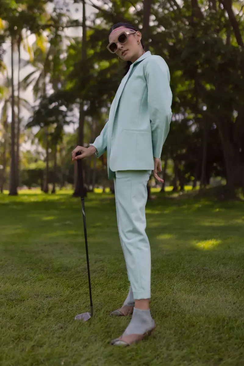 Woman in a pale green suit and sunglasses holding a golf club