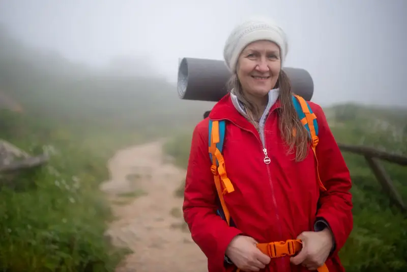 Older woman hiking a misty trail in a red jacket and backpack