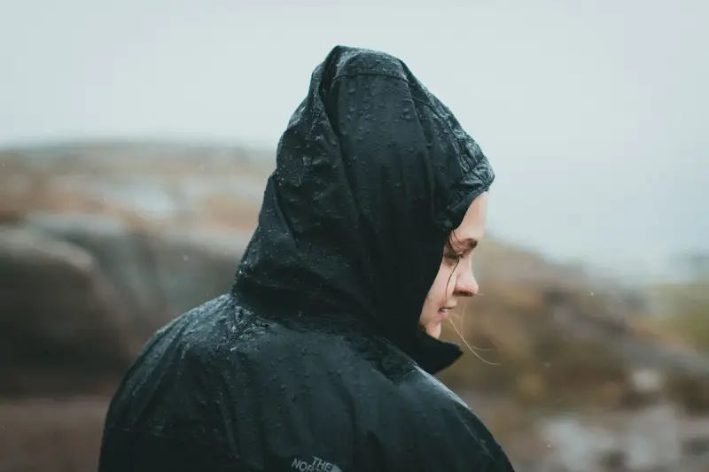 A woman in a rain jacket stands outdoors as rain falls