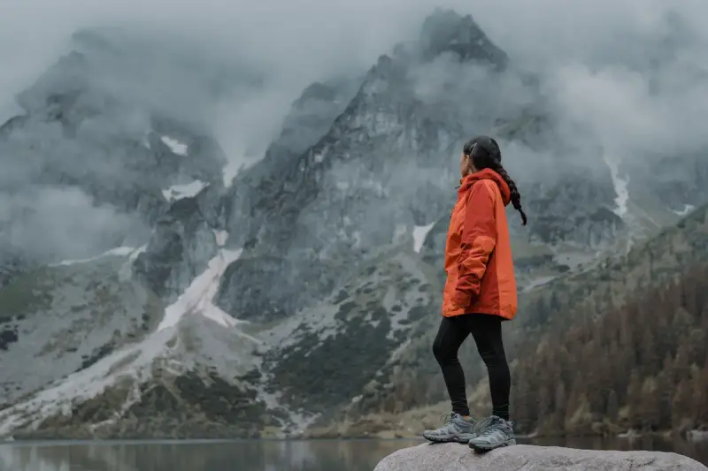 A woman in an orange jacket hikes across a foggy mountain ridge