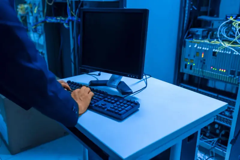 An IT professional works at a computer in a server room.