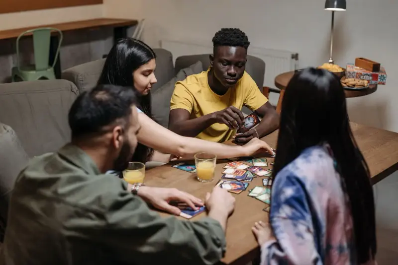 Four adults seated around a table laying down cards in a strategy card game