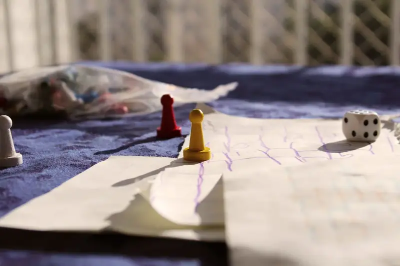 Two wooden pawns and a die on a hand-drawn paper game board in sunlight