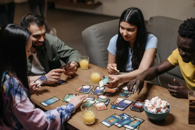 Friends sharing snacks and drinks while playing a colorful card game at a table