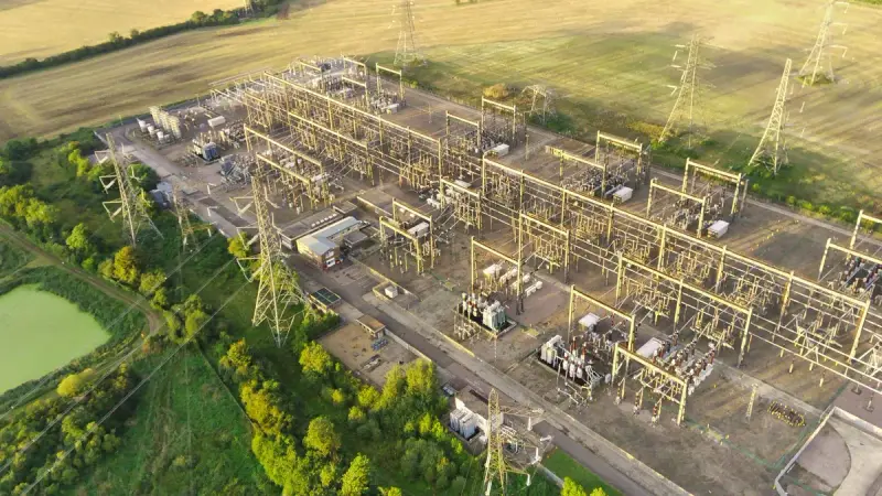 Aerial view of a large electrical substation with transmission towers beside green fields
