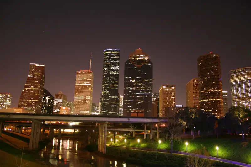 Downtown Houston skyscrapers lit up at night above Buffalo Bayou and its lit walking paths