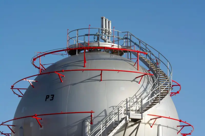 Close-up of a gas storage sphere with red spiral stairs and safety rails