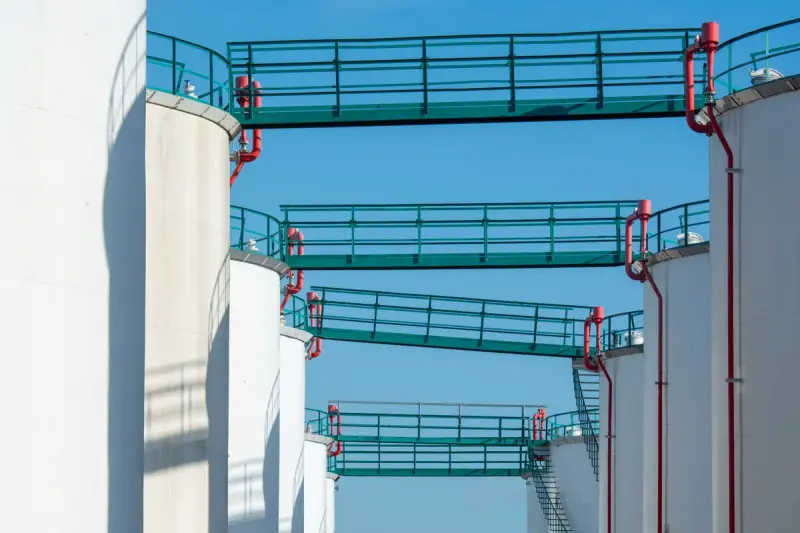 White storage tanks linked by teal walkways against a blue sky
