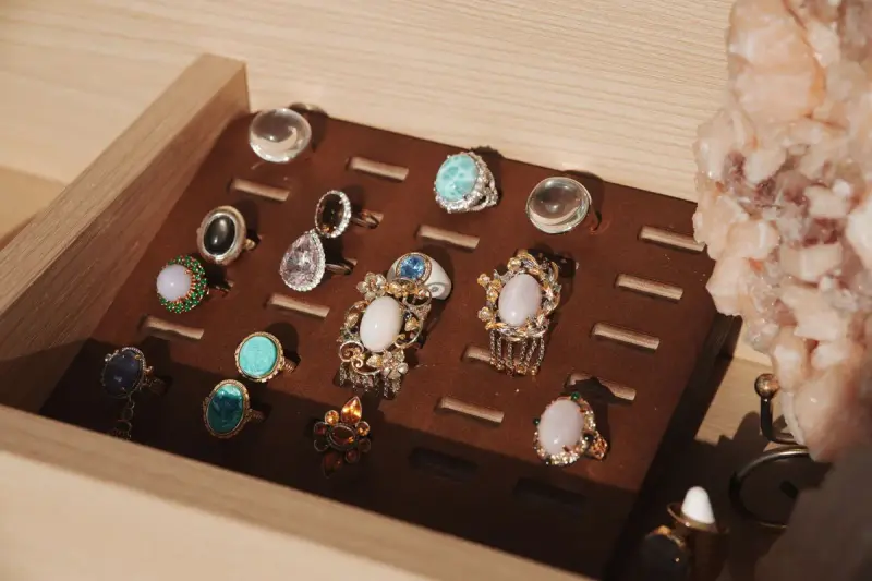 Gemstone rings lined up in a brown jewelry tray beside a natural crystal