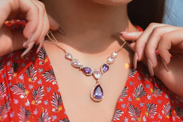 A woman fastening a purple gemstone pendant necklace