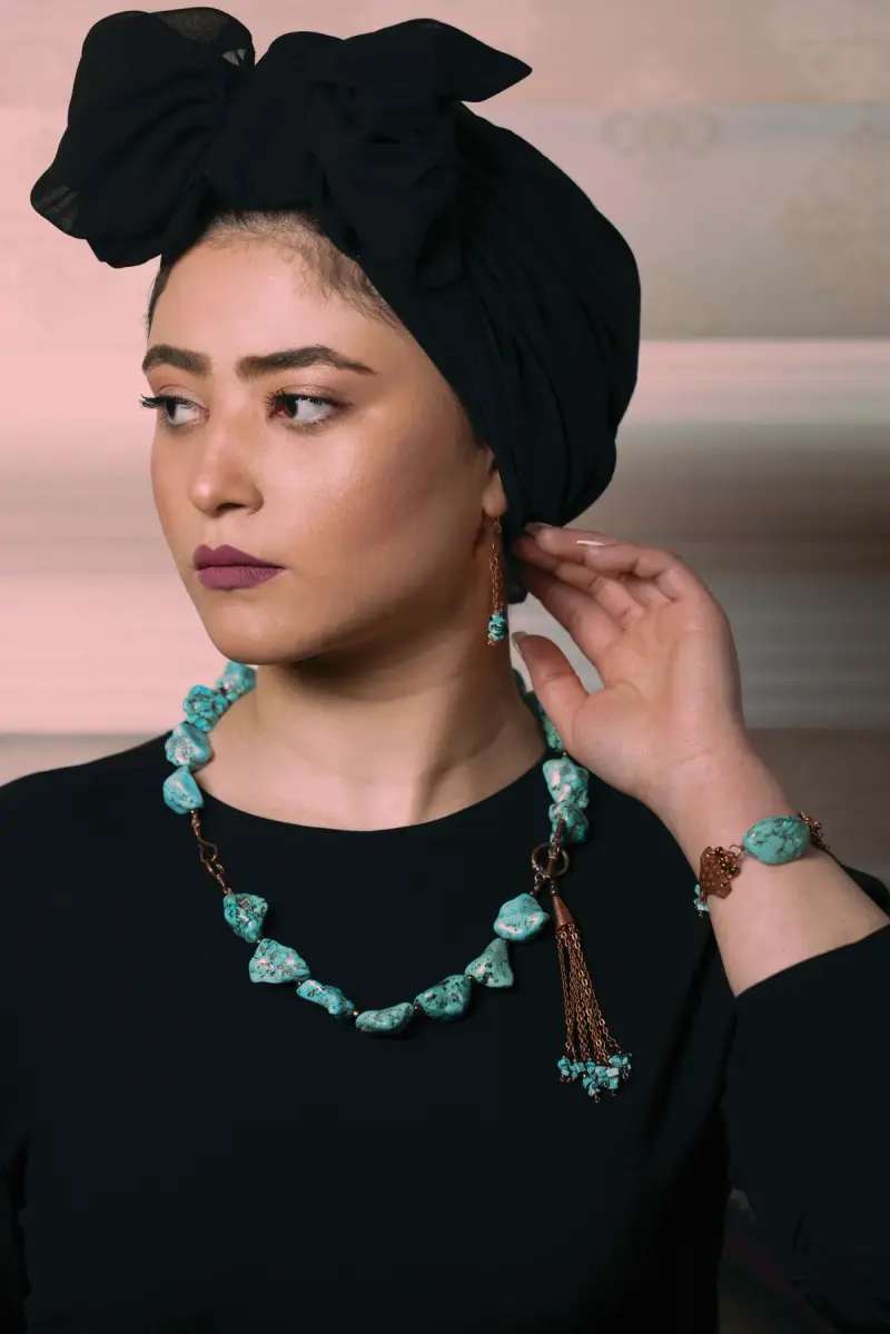 Woman in a black headscarf and top wearing a raw turquoise necklace and bracelet