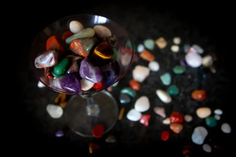 Polished semi-precious stones spilling from a glass onto a black surface