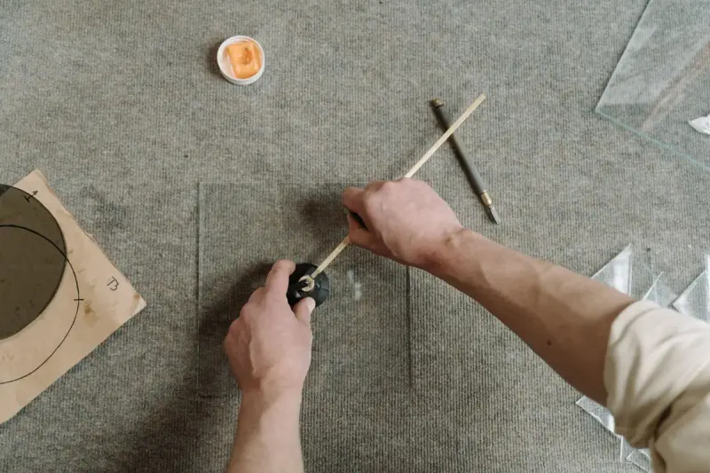 Overhead view of hands scoring a curve into a glass pane with a hand cutter
