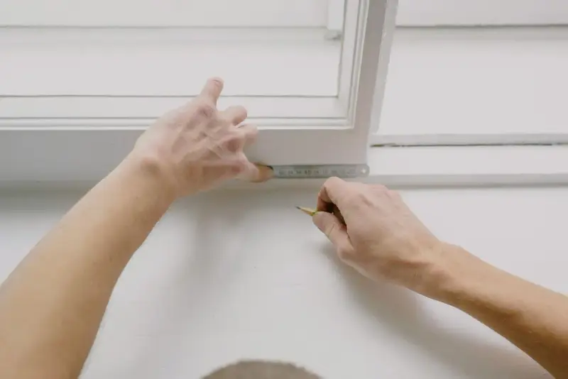 Installer measuring a white window frame opening with a steel ruler
