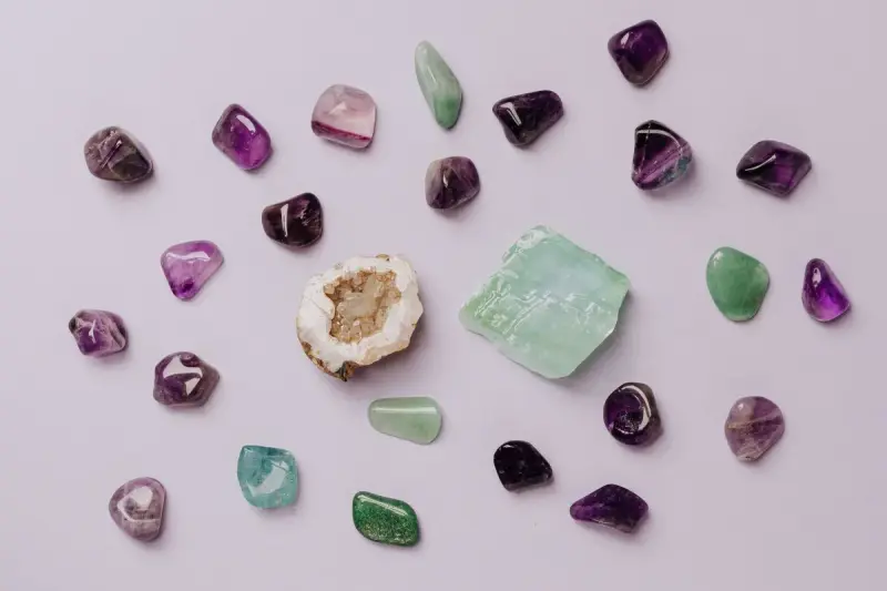 Flat lay of small polished amethyst, jade and quartz stones with a geode half on lilac paper