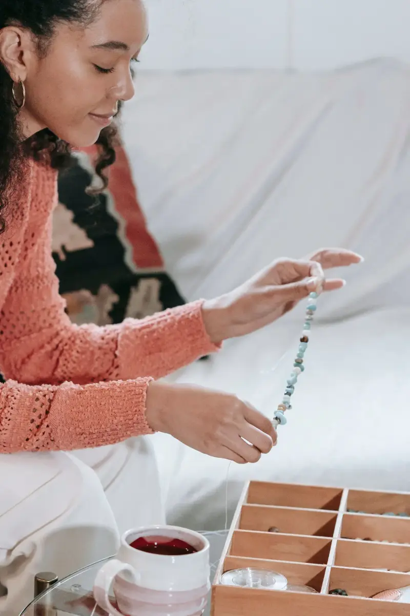 Woman stringing turquoise and stone beads into a bracelet beside a wooden bead tray