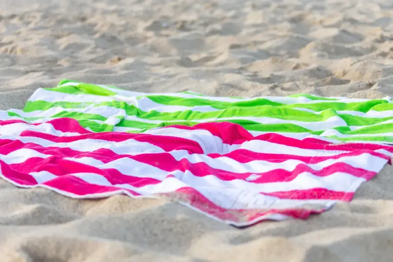 Green and pink striped beach towels spread on the sand