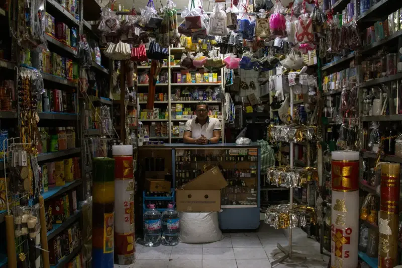 Shopkeeper behind the counter of a small store packed with assorted products