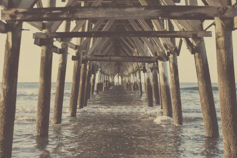 View beneath a wooden pier in North Myrtle Beach with rows of pilings